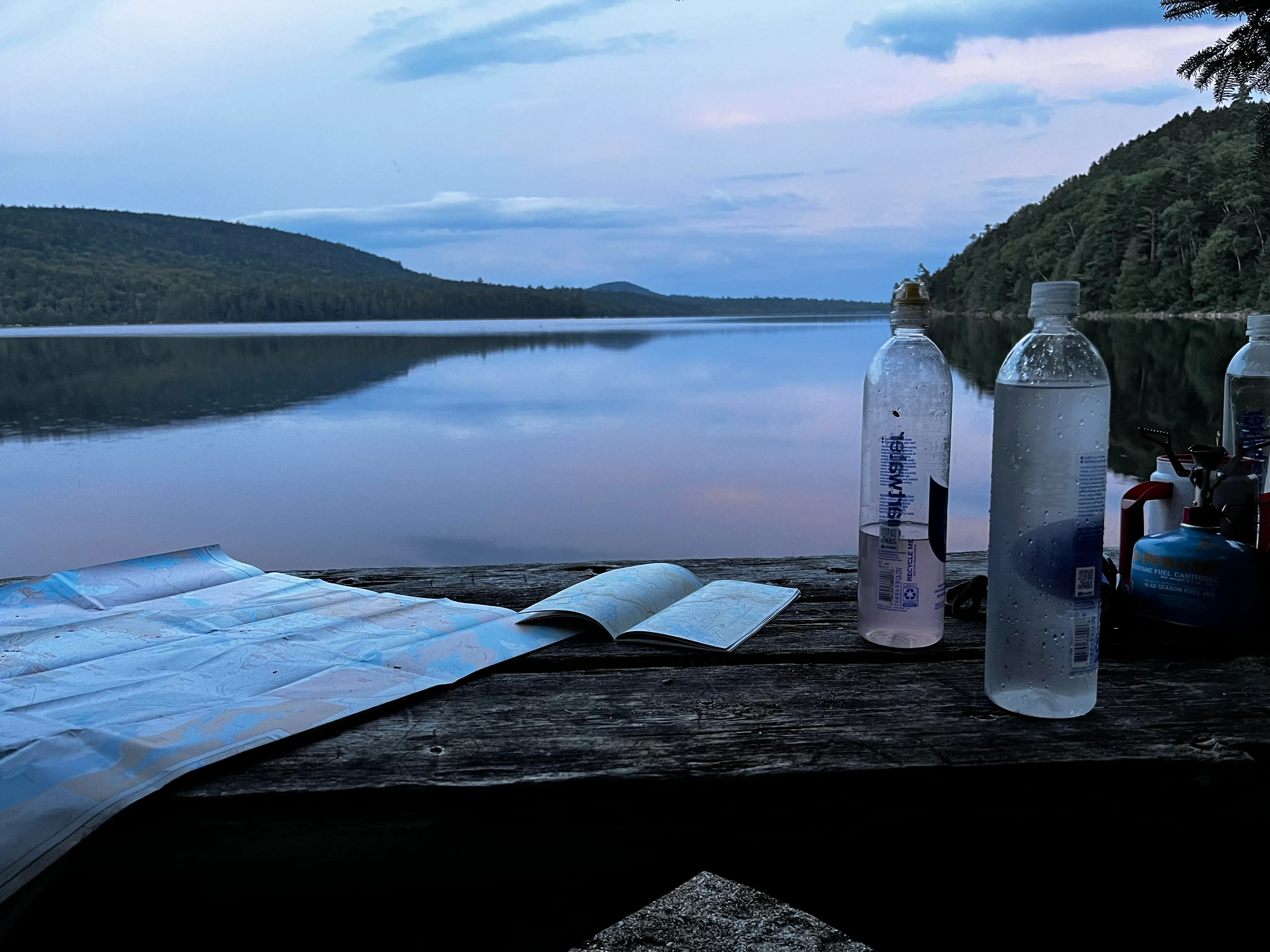 Sunset over a lake Maps and water bottles spread across a picnic table by a lake at sunset